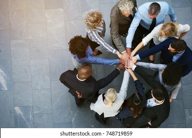 High angle view of a team of united coworkers standing with their hands together in a huddle in the lobby of a modern office building