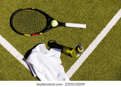 High angle view tennis racket with ball, water bottle and napkin over grassy field in tennis court. Copy space, unaltered, sport, competition, green and summer concept. - Powered by Shutterstock