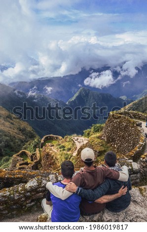 High angle view of three backpacker male friends hugging each other on Phuyupatamarca ruins with the huge valley in front of them. Inca trail to Machu Picchu in Peru. South America