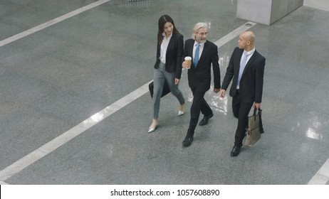 High Angle View Of Three Corporate Executives Talking While Walking Across Lobby Of Modern Office Building.