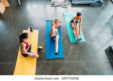 high angle view of three multiethnic sportswomen exercising on fitness mats at gym