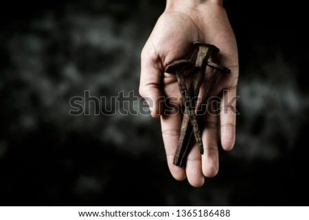 high angle view of three rusty nails, depicting the holy nails of the cross of Jesus Christ, on the hand of a man, on a dark background, with some blank space on the left