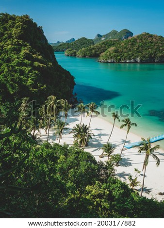High angle view through coconut tree to white sand beach surrounded with limestone islands and emerald green water in summer. Mu Koh Ang Thong National Marine Park, near Koh Samui, Thailand.