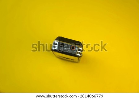 High angle view of the top panel of a digital voice recorder showing a black headphone jack and a red microphone jack input, isolated on a bright yellow background. Concept of audio connectivity, sound hardware, journalism and recording equipment.