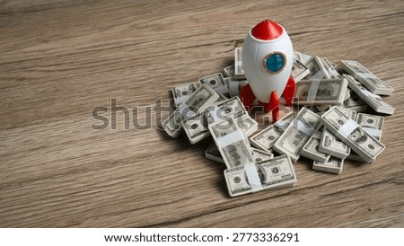 High angle view of a toy rocket surrounded by stacks of hundred dollar bills signifying financial prosperity.