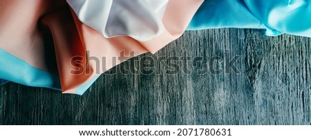 high angle view of a transgender pride flag draped on a rustic gray wooden surface, in a panoramic format to use as web banner or header