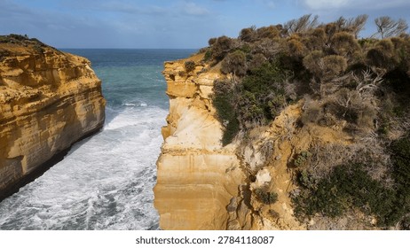 High angle view of turquoise waves crashing between steep sandstone cliffs under bright daylight