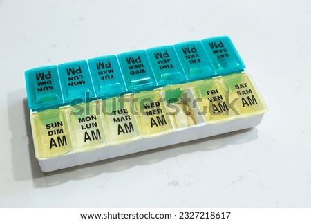 High angle view of turquoise and yellow two-week pillbox labelled with the days of the week in English and French, and with one compartment open
