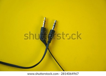 High angle view of two black 3.5mm audio jack connectors, one TRRS with a gold tip and one TRS with a silver tip, isolated on a bright yellow background. Concept of sound, music, and media hardware.