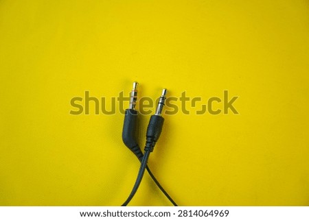 High angle view of two black 3.5mm audio jack connectors, one TRRS with a gold tip and one TRS with a silver tip, isolated on a bright yellow background. Concept of sound, music, and media hardware.