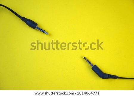 High angle view of two black 3.5mm audio jack connectors, one TRRS with a gold tip and one TRS with a silver tip, isolated on a bright yellow background. Concept of sound, music, and media hardware.