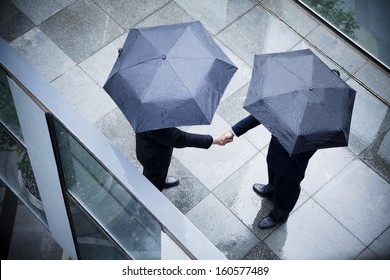 High angle view of two businessmen holding umbrellas and shaking hands in rain - Powered by Shutterstock