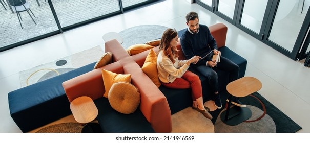 High angle view of two businesspeople working in an office lobby. Two modern businesspeople using a digital tablet while having a discussion. Two young entrepreneurs collaborating on a new project.