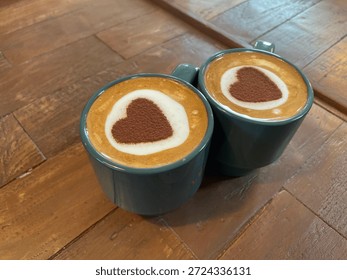 High angle view of two coffee mugs with heart shaped cocoa powder art on rustic wooden table