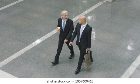 high angle view of two corporate executives talking while walking across lobby of modern office building. - Powered by Shutterstock