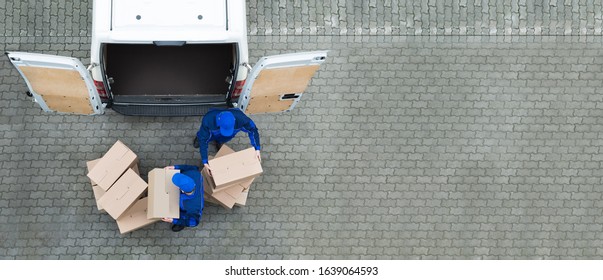 High Angle View Of Two Delivery Men Unloading Cardboard Box From Truck
