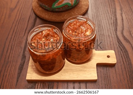 High angle view of two jars of homemade squid chili sauce rich in spices, applicable for spicy food promotions, recipe blogs, or online product catalogs showcasing Indonesian-style condiments