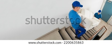 High Angle View Of Two Male Movers Carrying Sofa On Staircase Of House