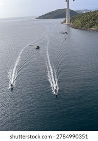 High angle view of two motorized boats cruising in formation on deep blue ocean water. The fast-moving vessels leave long, prominent white wakes behind them in the sea.