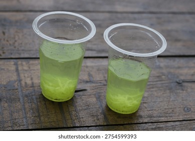 High angle view of two plastic cups containing fresh lime or cucumber drinks with shredded fruit inside on a weathered wooden table.