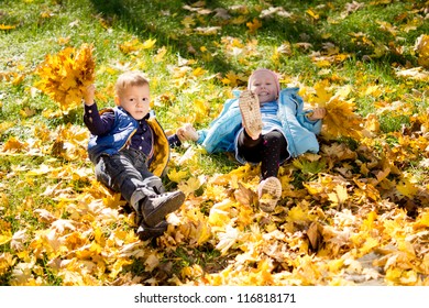 High angle view of two young kids frolicking in yellow autumn leaves that have fallen onto the grass