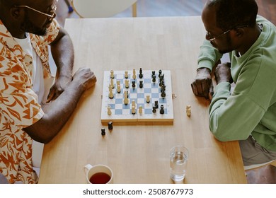 High angle view of two young African American men sitting at wooden table playing chess game and talking