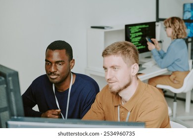 High angle view of two young ethnically diverse programmers working together on new software in modern IT company office