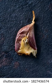 High Angle View Of An Unpeeled Roasted Garlic Clove On A Black Stone Surface