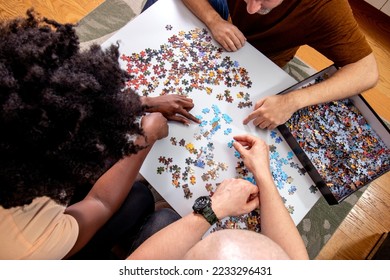 High Angle View of an unrecognizable family playing a jigsaw puzzle game together at home. Putting things together and solving problems. Fun and diversity in friendship. - Shutterstock ID 2233296431