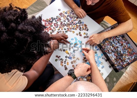 High Angle View of an unrecognizable family playing a jigsaw puzzle game together at home. Putting things together and solving problems. Fun and diversity in friendship.