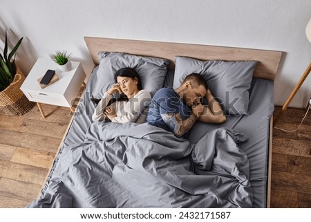 high angle view of upset multiethnic couple lying down on bed at home, family divorce concept
