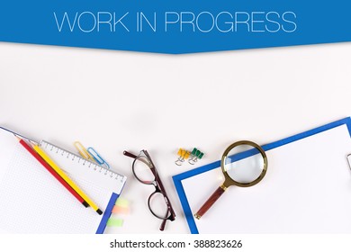 High angle view of various office supplies on desk with a word WORK IN PROGRESS - Powered by Shutterstock