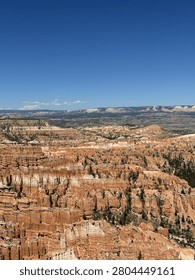 High angle view of the vast Bryce Canyon amphitheater with unique orange hoodoos and green pine trees under a clear blue sky, Utah, USA.