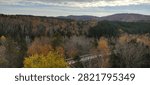 High angle view of a vast mountain valley covered in colorful autumn forest with a wooden boardwalk structure peeking through the canopy in Quebec, Canada.