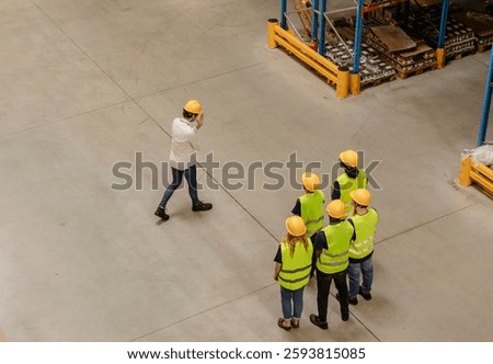 High angle view of a warehouse manager guiding a group of workers during a training session, emphasizing teamwork, safety, and efficiency in logistics operations