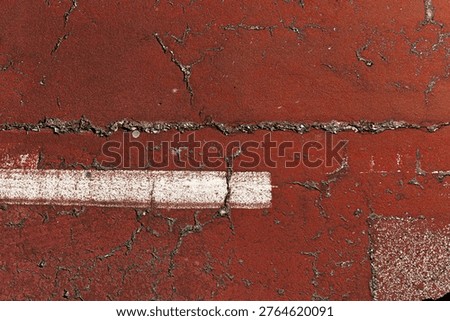 High angle view of a weathered red athletic running track or sports court featuring deep cracks and a white painted line. Stock photo