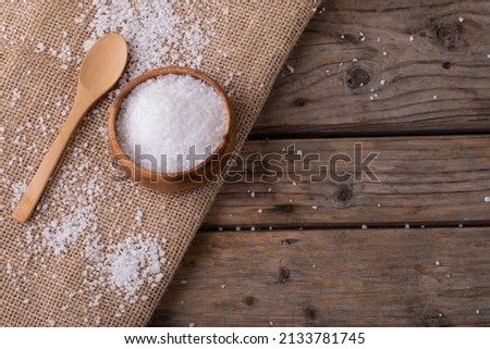 High angle view of white rock salt in wooden bowl by spoon on jute fabric at table. unaltered, ingredient, food, rock salt and seasoning.