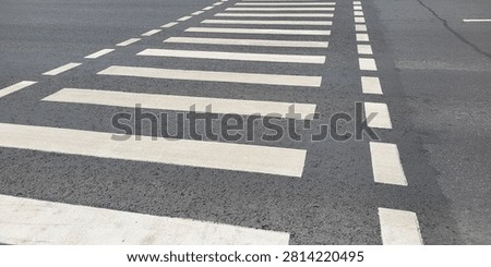 High angle view of a wide white zebra pedestrian crossing with dotted boundary lines painted on a grey asphalt road surface