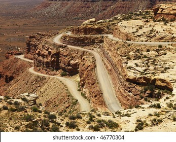 High Angle View Of A Winding Dirt Road On A Desert Rock Formation. The Surrounding Landscape Is Visible In The Background. Horizontal Shot.