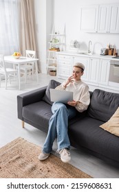 High Angle View Of Woman In Jeans Sitting With Laptop On Sofa In Open Plan Kitchen