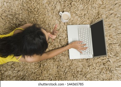 High Angle View Of A Woman Lying On A Rug And Working On A Laptop