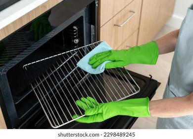High angle view of woman in rubber gloves cleans the grill grid inside oven. Female using a cloth to wipe household appliance inregrated in kitchen. Housework and cleaning service concepts - Shutterstock ID 2298489245