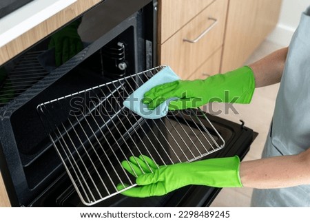 High angle view of woman in rubber gloves cleans the grill grid inside oven. Female using a cloth to wipe household appliance inregrated in kitchen. Housework and cleaning service concepts