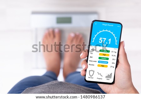 High Angle View Of A Woman Standing On Weighing Scale Holding Cellphone