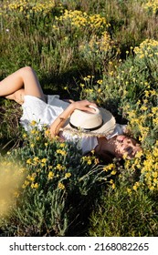 High Angle View Of Woman In Summer Dress Holding Sun Hat While Lying On Meadow