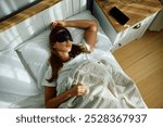 High angle view of woman wearing sleeping eye mask in bed.