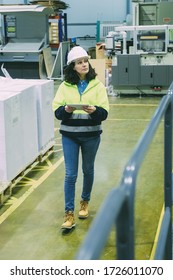 High Angle View Of Worker Using Tablet While Walking At Factory. Focused Mature Woman Checking Equipment At Printing House. Print Manufacturing Concept