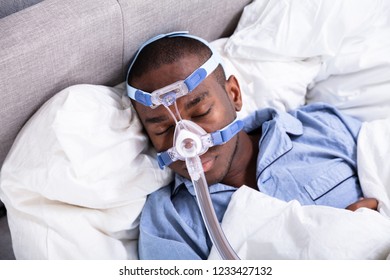 High Angle View Of A Young African Man Wearing CPAP Mask Sleeping On Bed