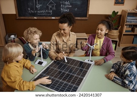 High angle view at young African American woman showing solar panel to group of little children in class explaining eco friendly energy