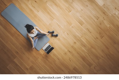 High angle view of young Asian woman practicing yoga and meditation at home sitting on floor in living room in lotus position with laptop and dumbbell. Mindful meditation and wellbeing concept - Powered by Shutterstock